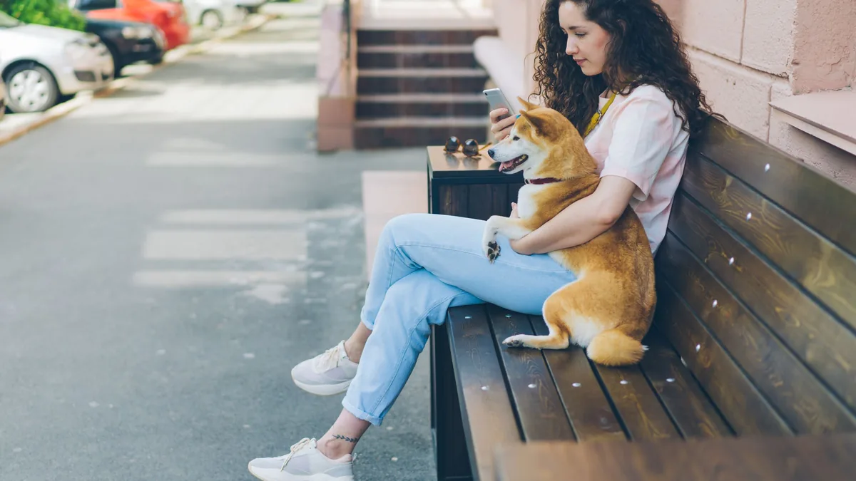 Femme assise en ville consultant son smartphone à côté de son chien